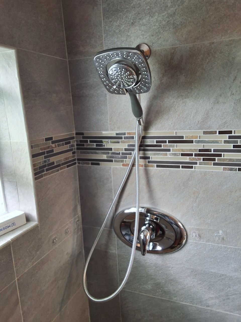 Chrome showerhead and hose mounted in a tiled bathroom shower corner.