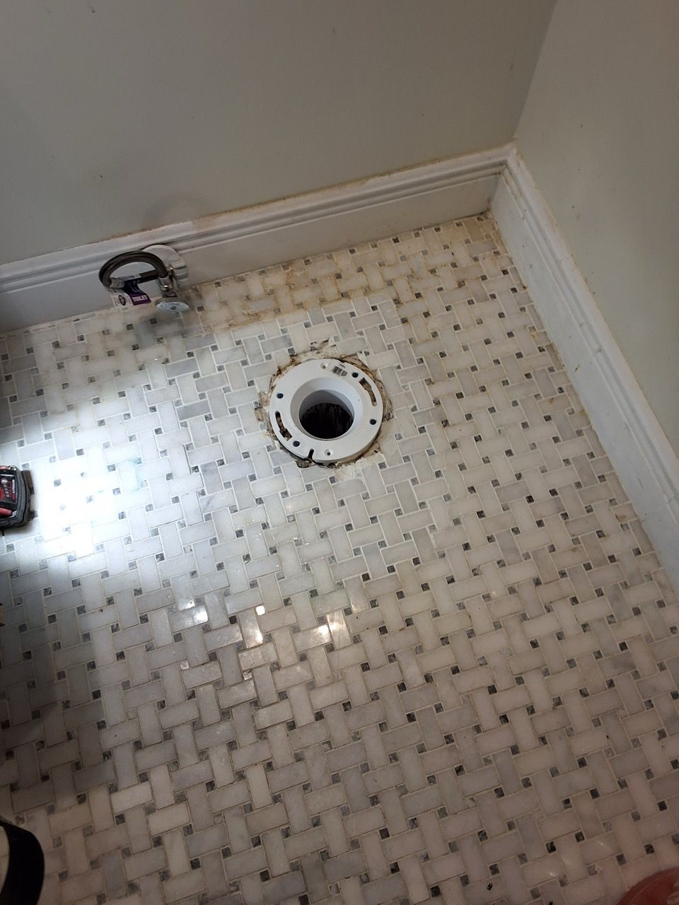 Small tiled shower floor with a central drain and white walls, viewed from above.