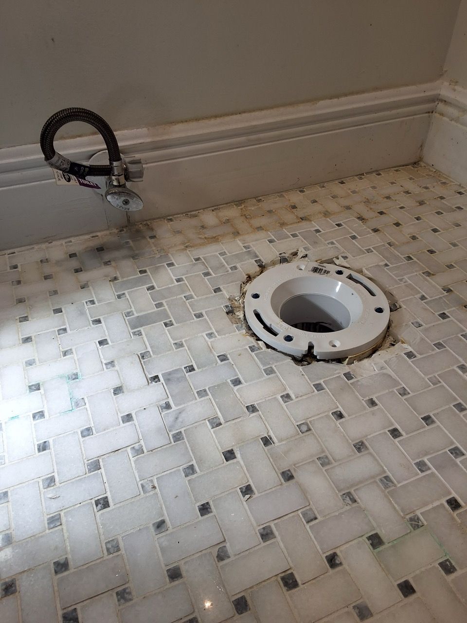 Bathroom floor with an open toilet drain and a detached black hose against the wall.