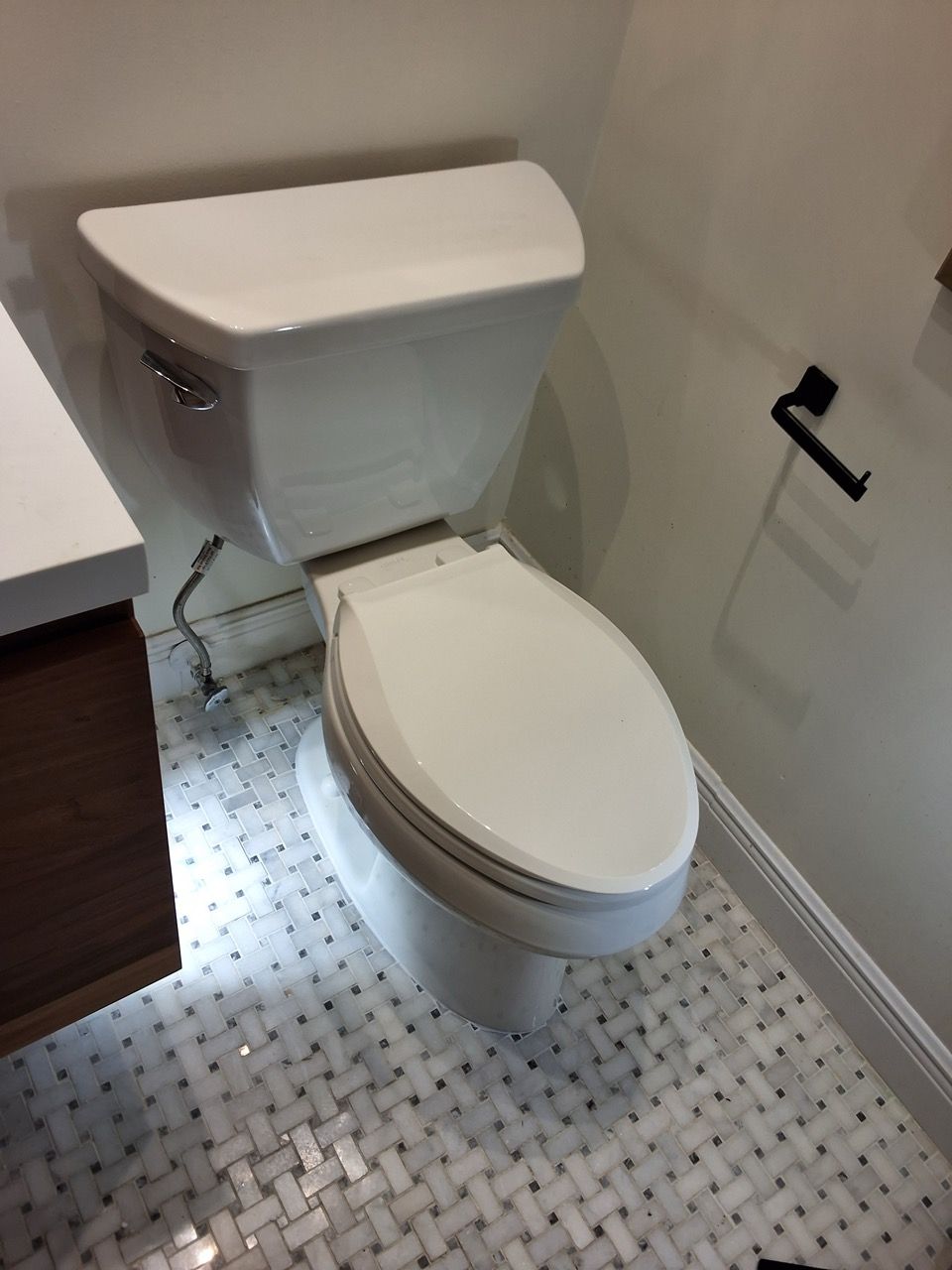 Compact white toilet in a small tiled bathroom with a grab bar on the wall.