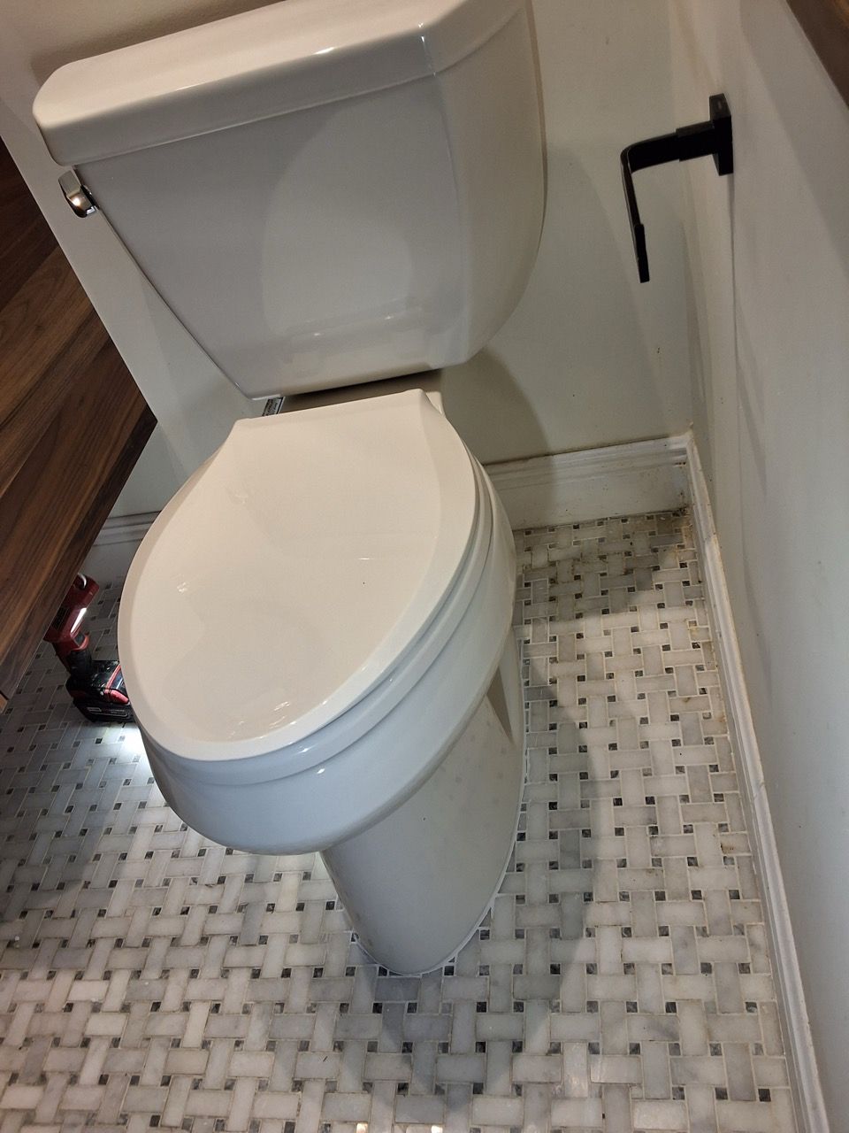 Compact white toilet in a small bathroom with a mosaic tile floor.