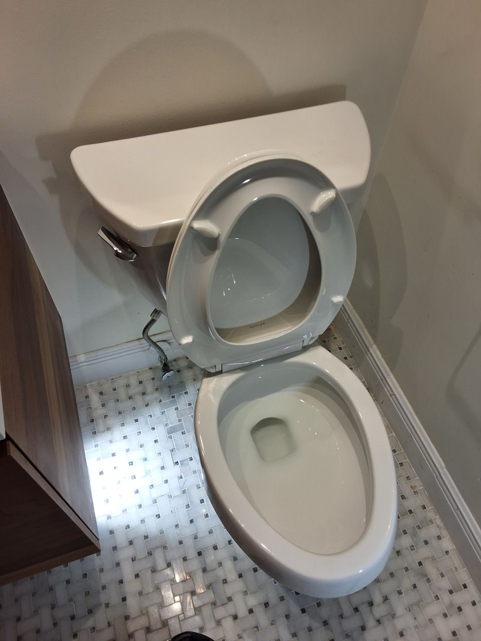 Small bathroom with an open toilet seat and lid next to a cabinet; patterned tile floor.