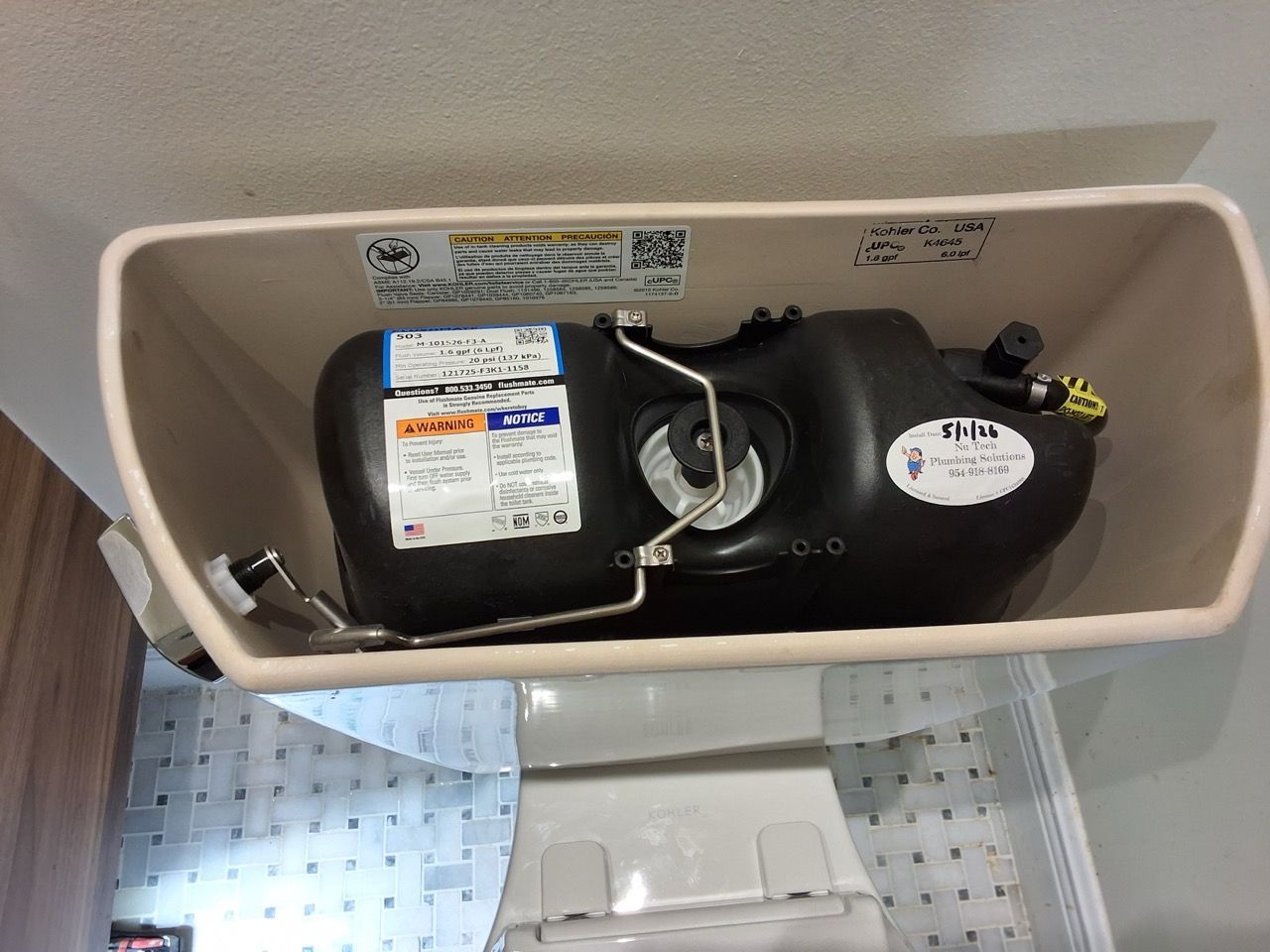 Open toilet tank showing black fill valve and internal plumbing components.