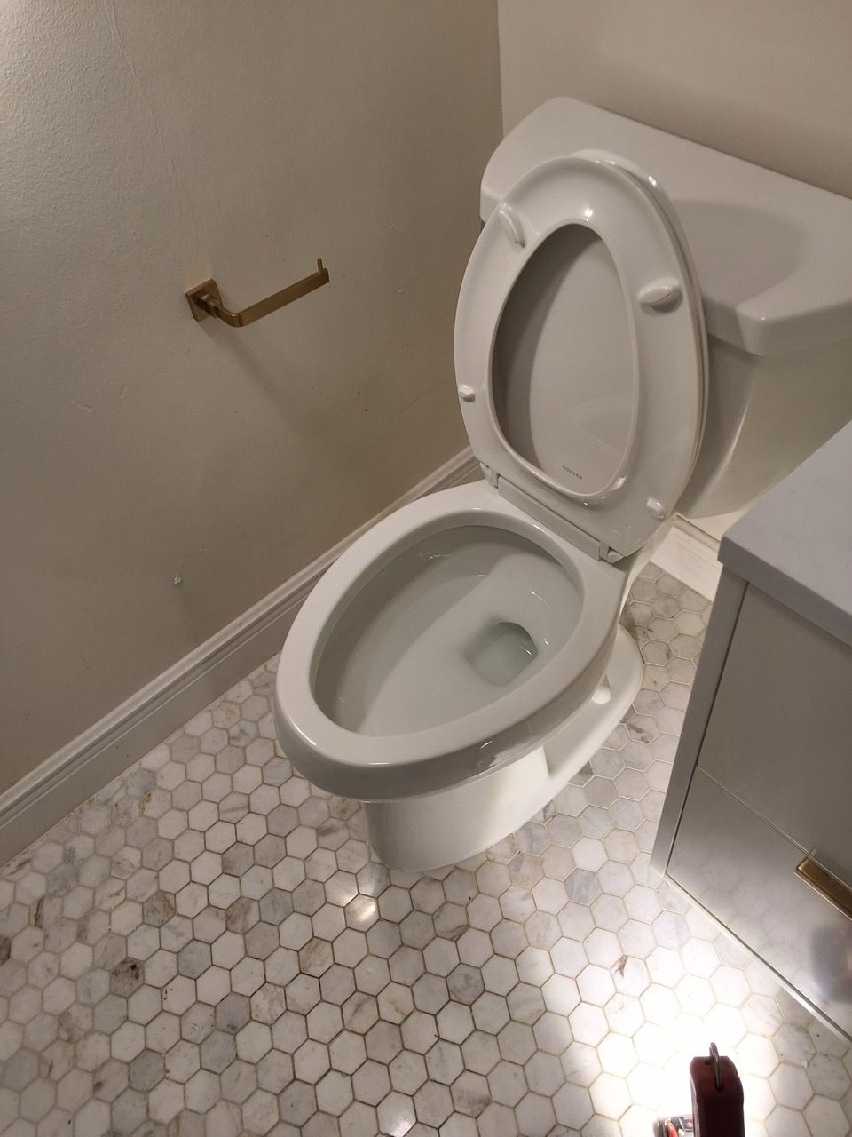 Small bathroom with open toilet, hex tile floor, and a damaged wall-mounted toilet paper holder.