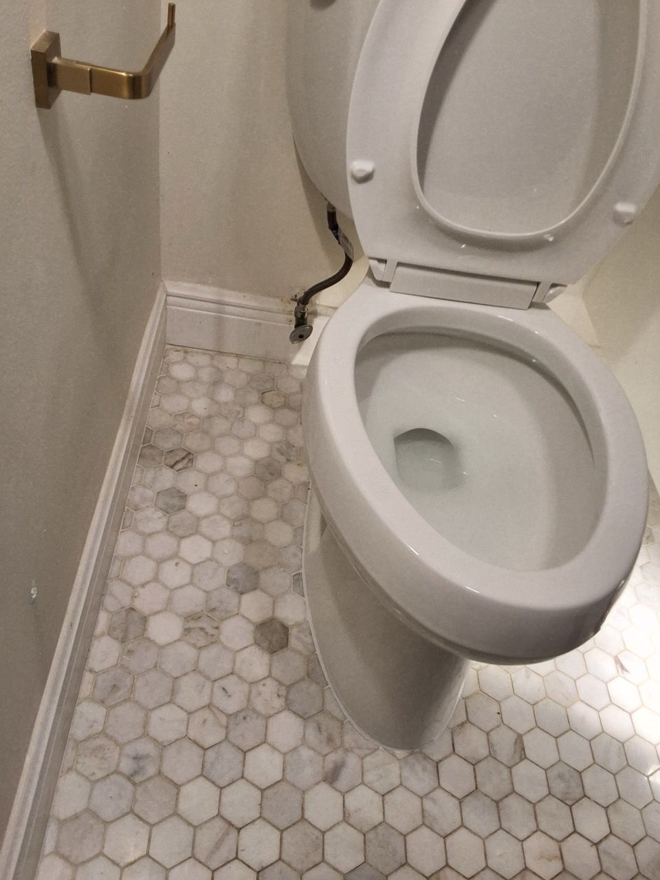 Bathroom with an open toilet beside a brass grab bar and hexagon tile floor.