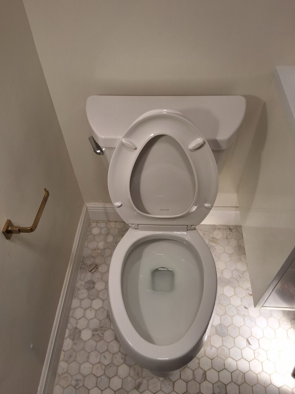Open toilet in a small bathroom with beige walls and hex tile floor.