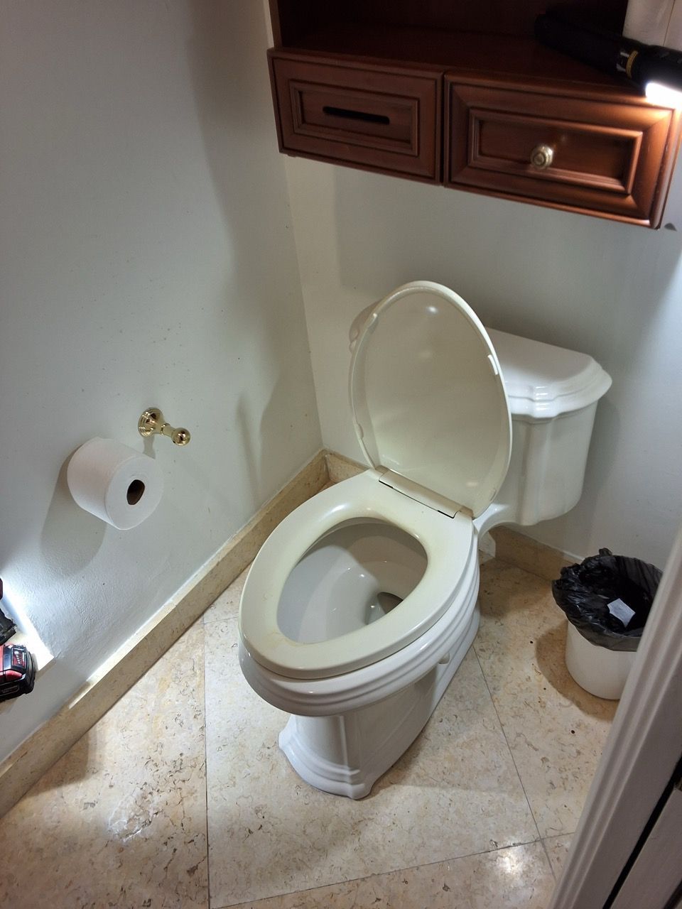 Small bathroom with toilet, wooden cabinet above, and toilet paper holder on the wall.
