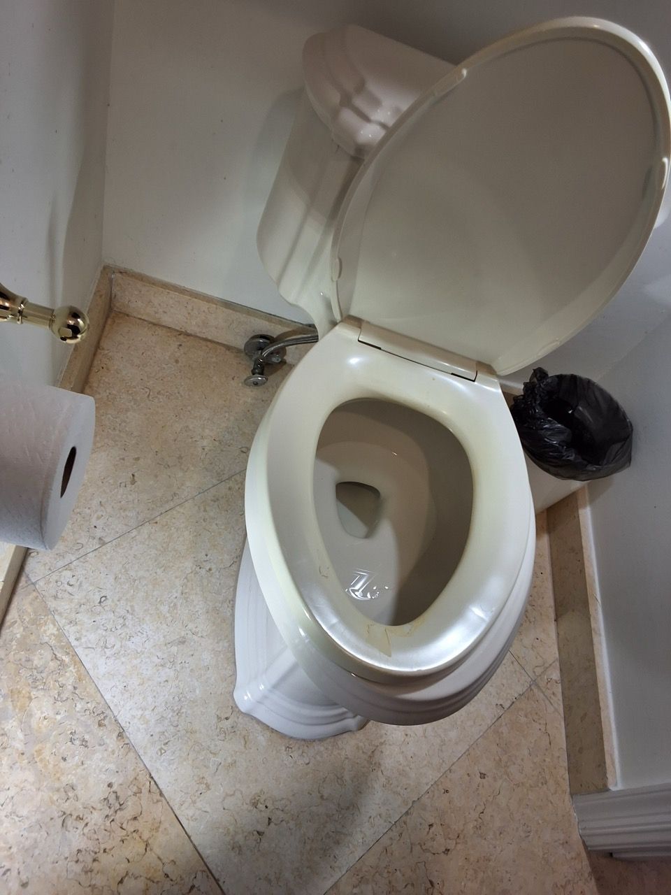 Open toilet in a small bathroom with beige tile floor and white walls.