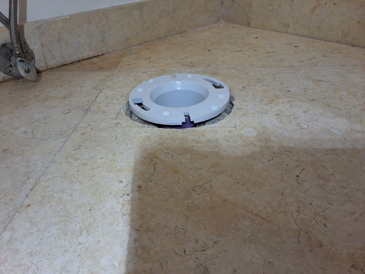 White circular floor drain cover on a beige tile floor near a wall corner
