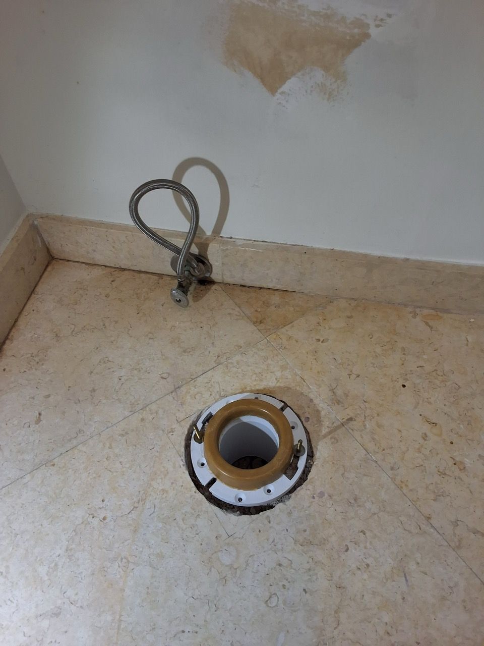 Small unfinished bathroom floor with a drain opening and exposed plumbing near the wall.