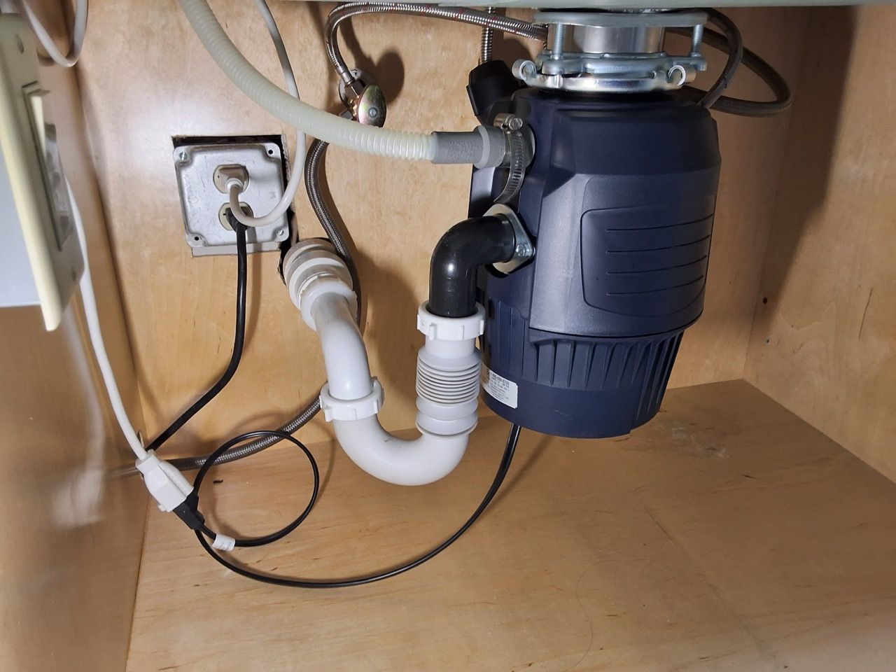 Under-sink garbage disposal and white PVC plumbing inside a cabinet