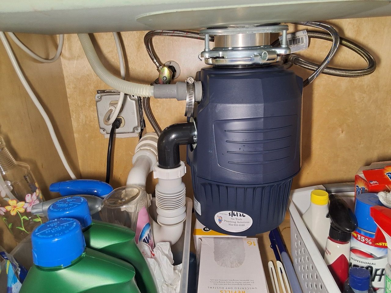 Under-sink garbage disposal and plumbing with cleaning supplies in a cabinet