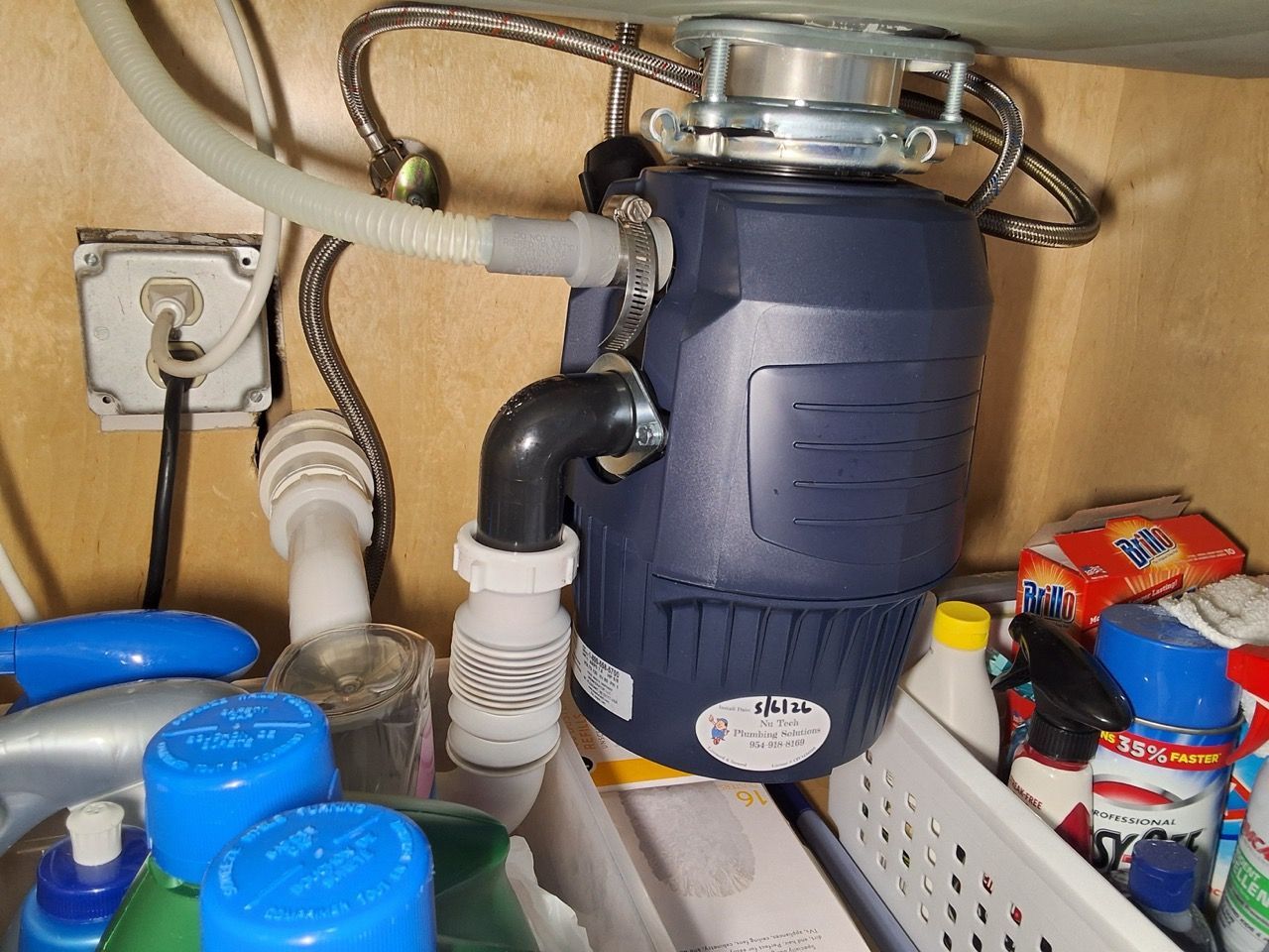 Under-sink garbage disposal with pipes, hoses, and cleaning supplies in a cabinet