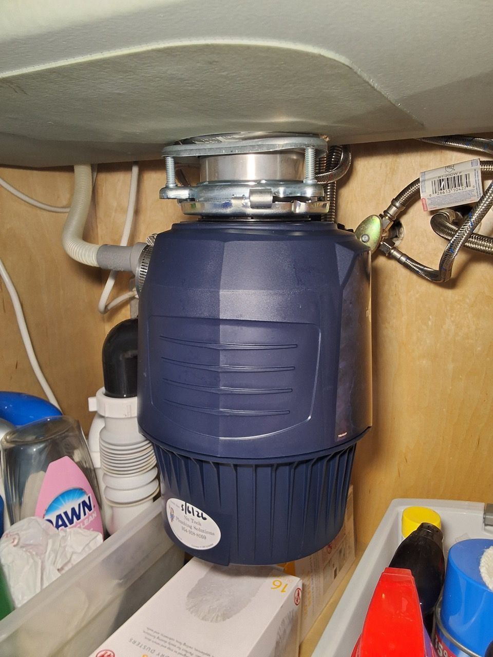 Under-sink blue garbage disposal unit with exposed plumbing and cords