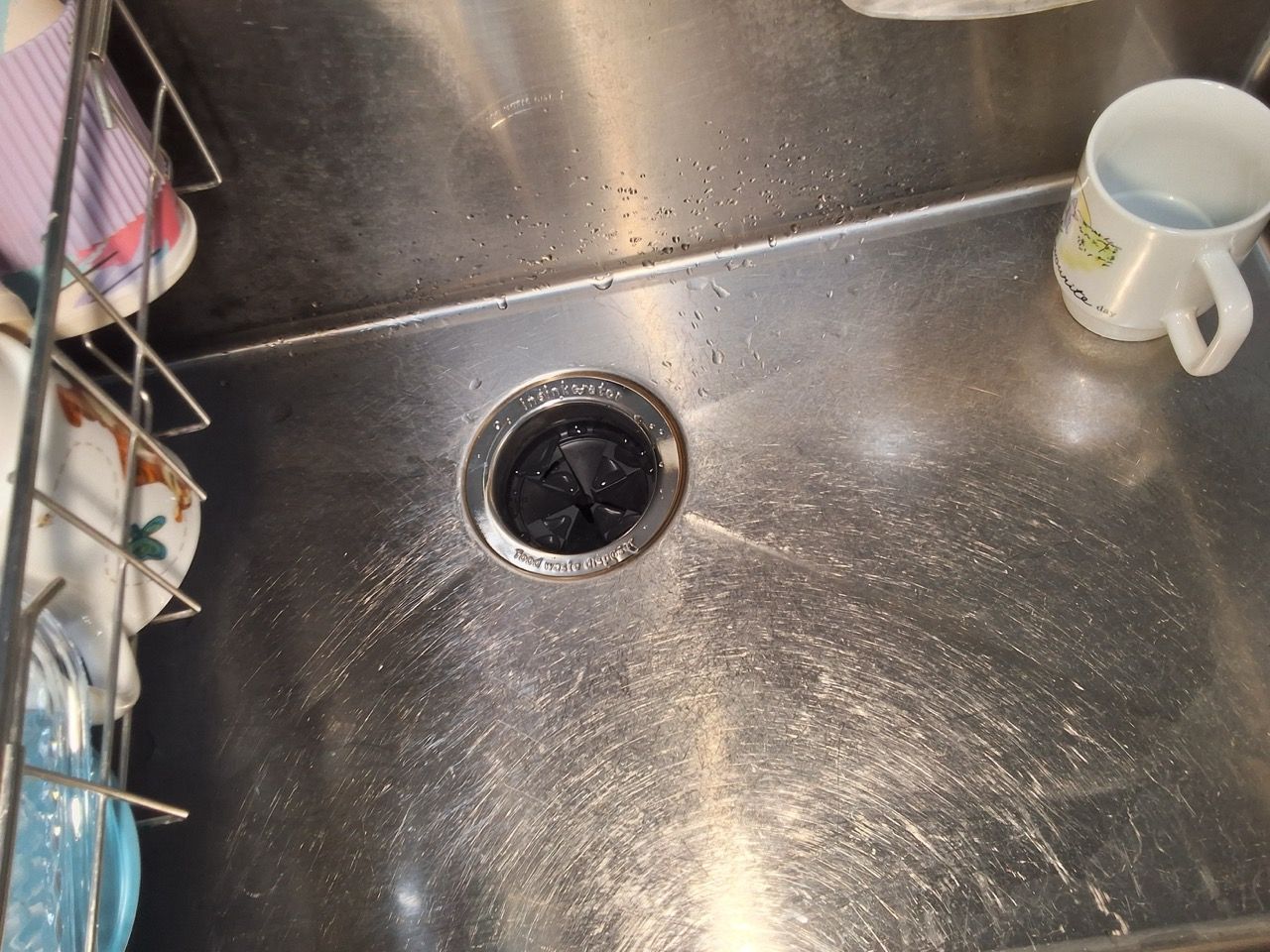 Kitchen sink with water splashed around the drain and a white mug on the right.