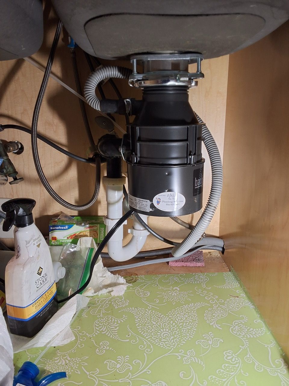 Under-sink garbage disposal and plumbing with cleaning spray bottle and green shelf liner