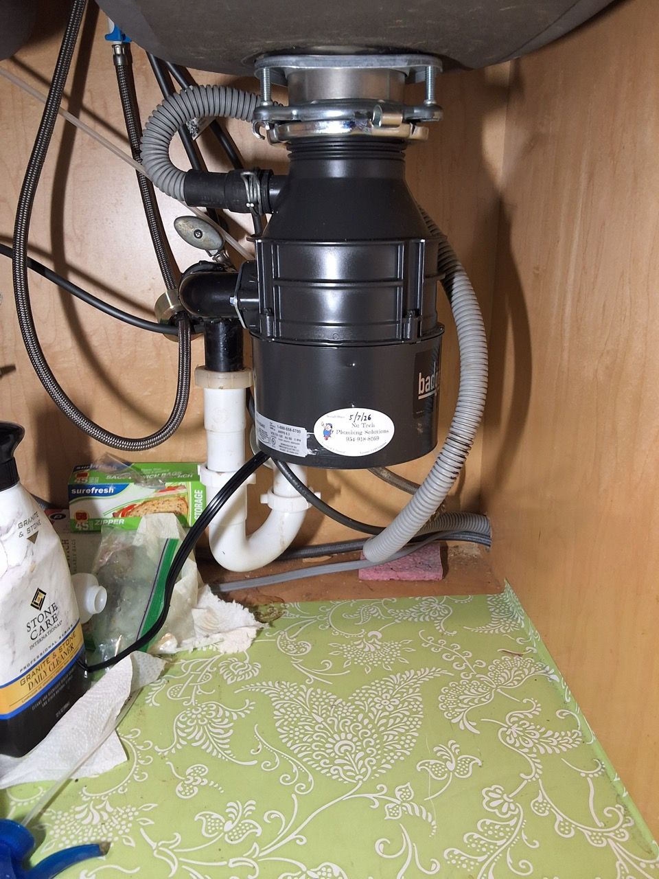 Under-sink garbage disposal and plumbing in a cabinet, with wires and cleaning items on the shelf