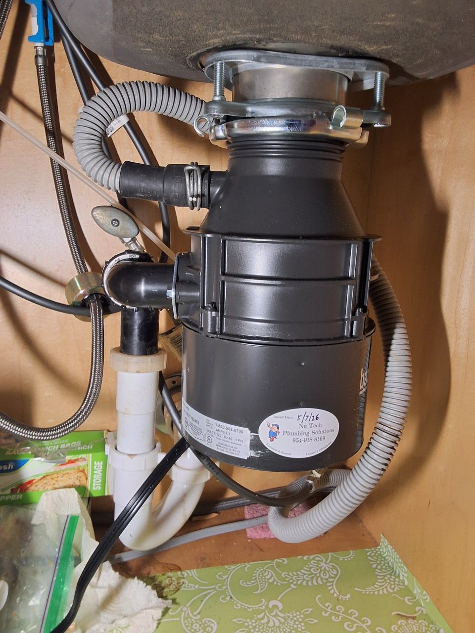 Under-sink garbage disposal with black drain pipes and flexible hoses in a cabinet.