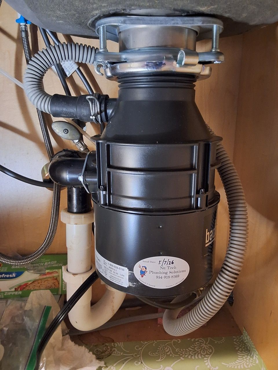 Under-sink garbage disposal unit with black motor housing and attached plumbing hoses