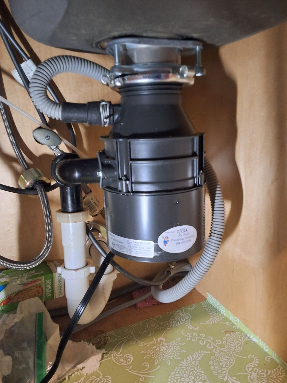 Under-sink garbage disposal and plumbing with black drain assembly and white pipe in a cabinet