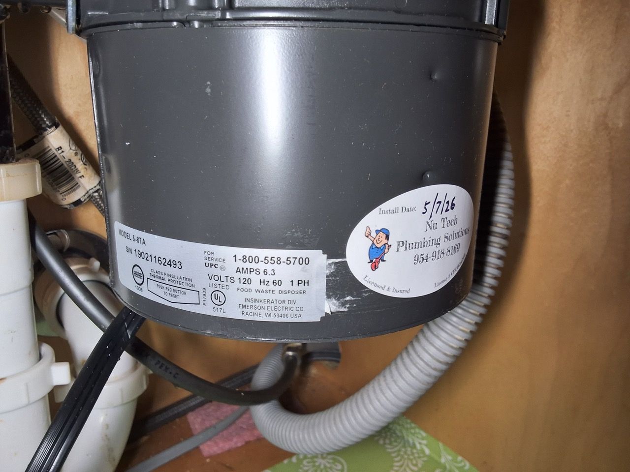 Close-up of a gray garbage disposal under a sink with wires and plumbing visible