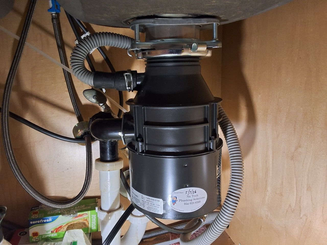 Under-sink garbage disposal and plumbing with black hoses and wires in a cabinet