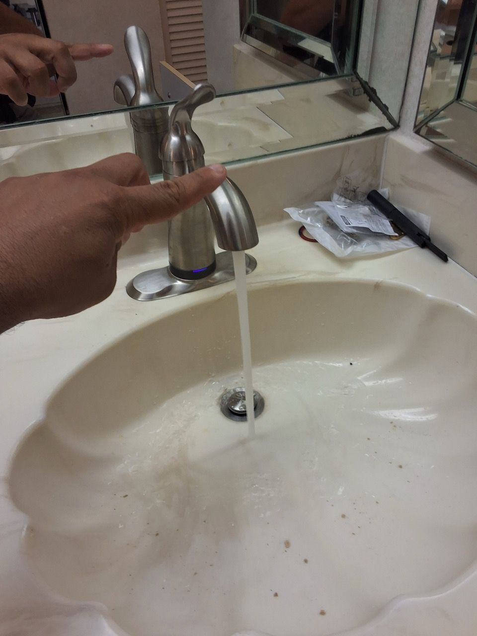 A hand turns on a bathroom faucet over a white sink, with water flowing into the drain.