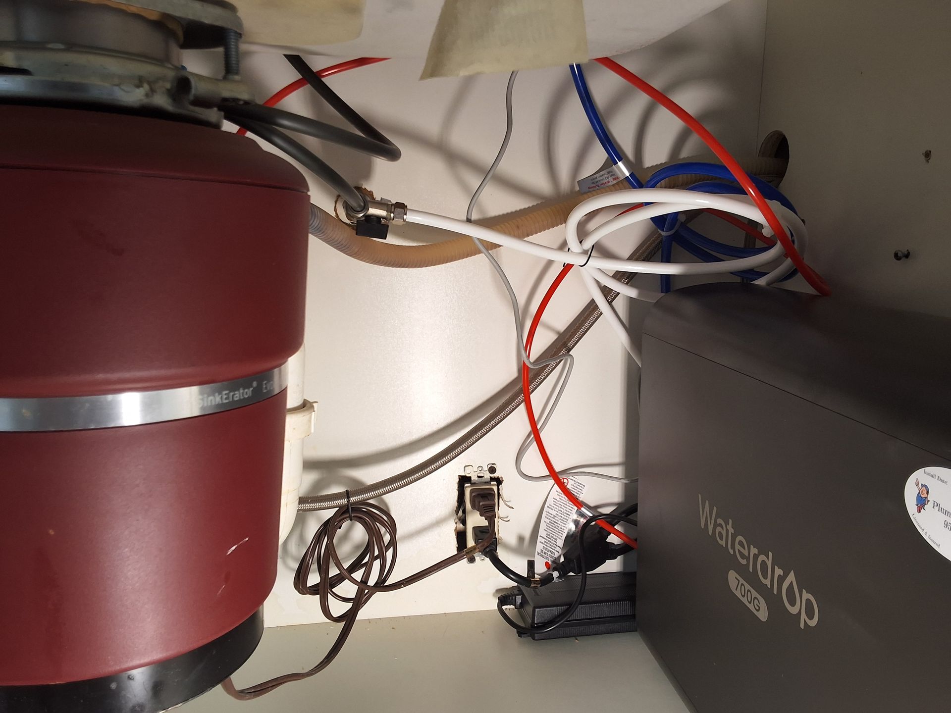 Wiring and cables inside a cabinet beside a red cylindrical tank and a black box.