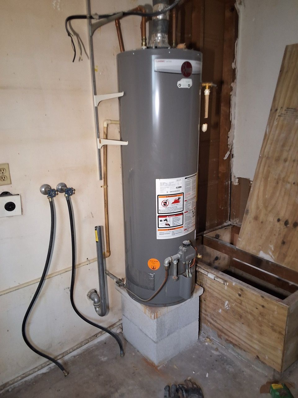 Gray water heater in unfinished utility room with exposed pipes and construction materials.