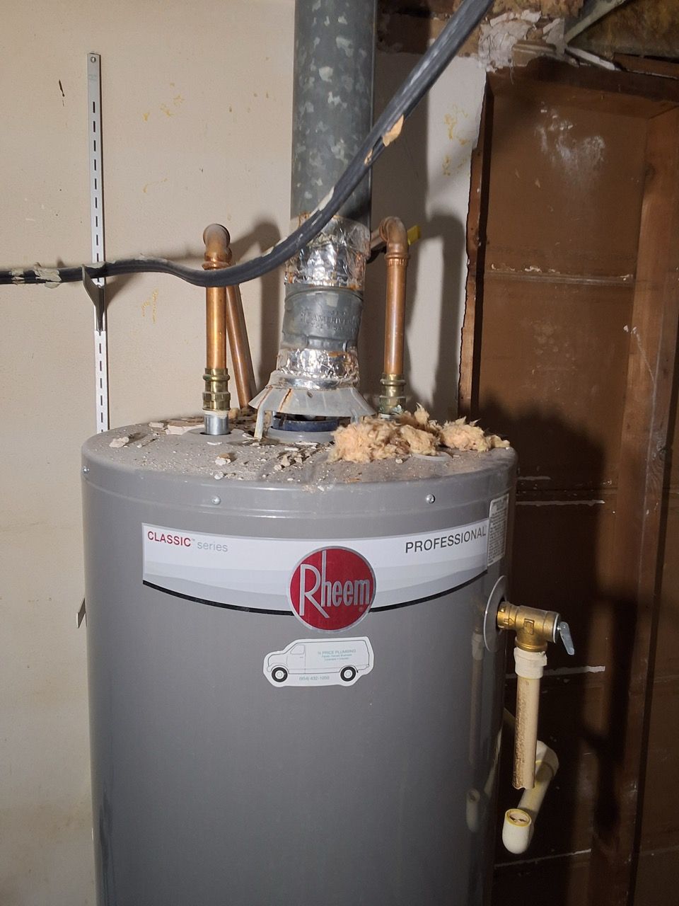 Gray Rheem water heater in a utility closet with pipes, venting, and insulation above it