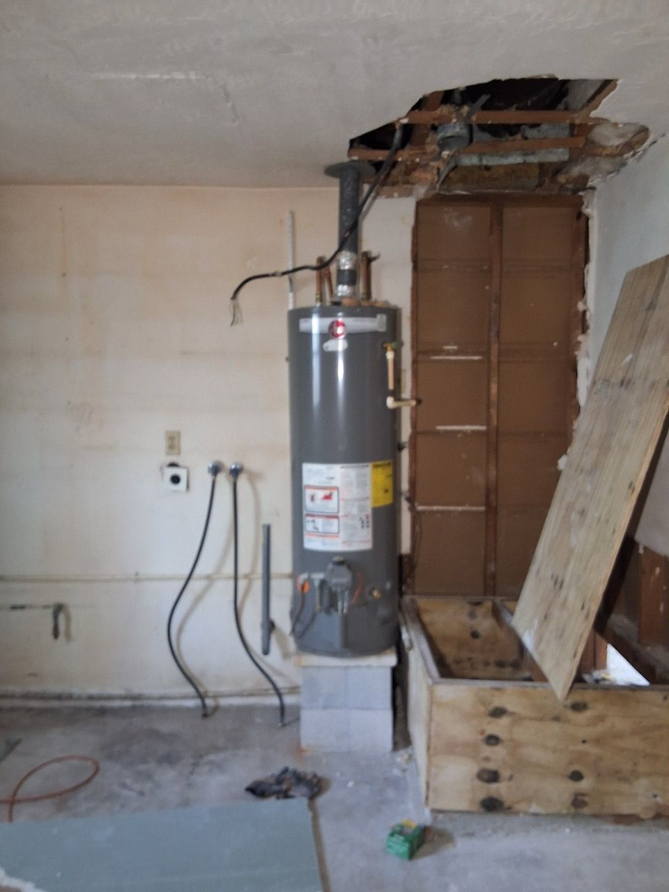 Damaged water heater in a garage with exposed ceiling and debris on the floor