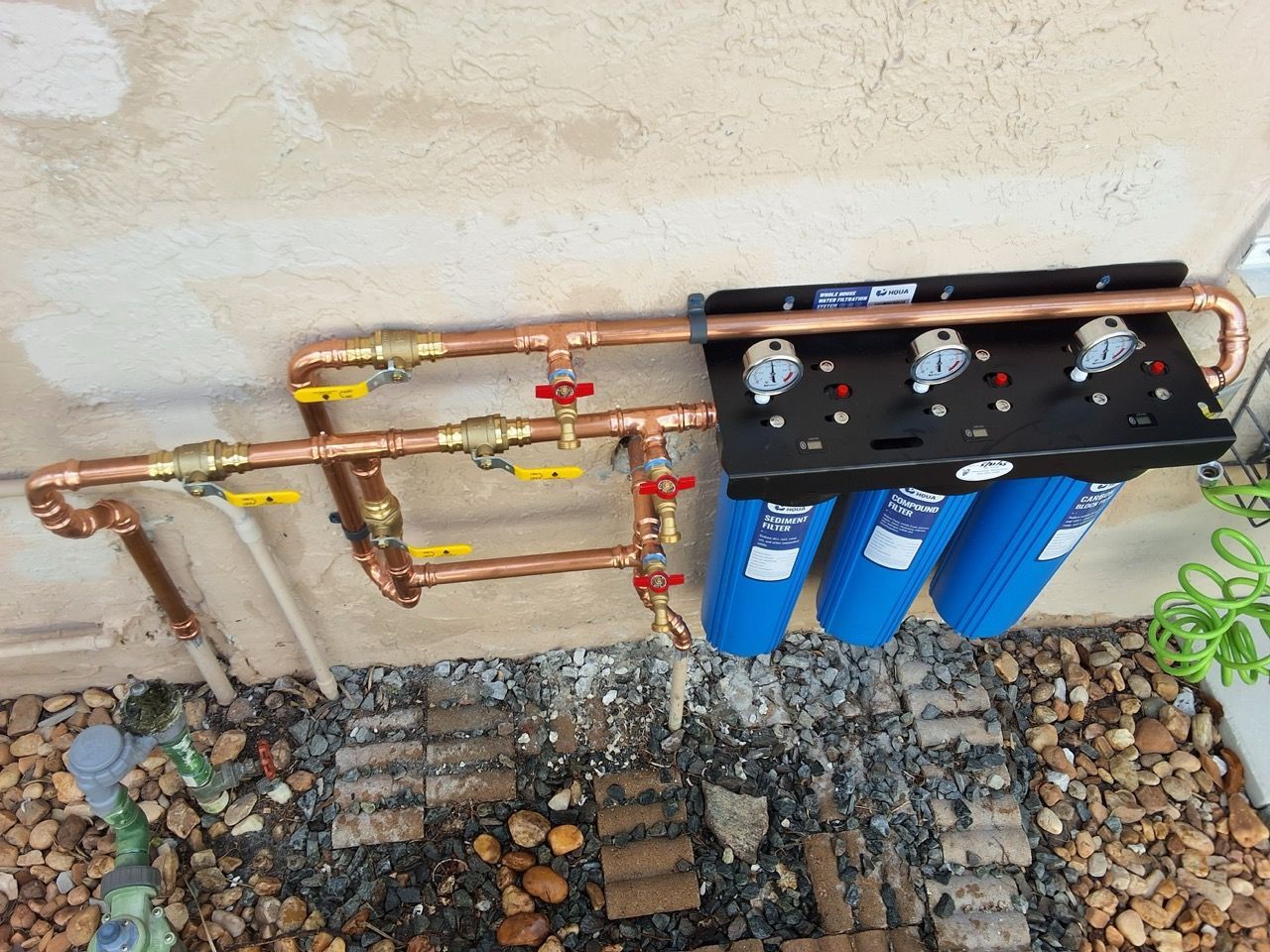 Water filtration system with copper pipes and blue filter canisters mounted on an exterior wall