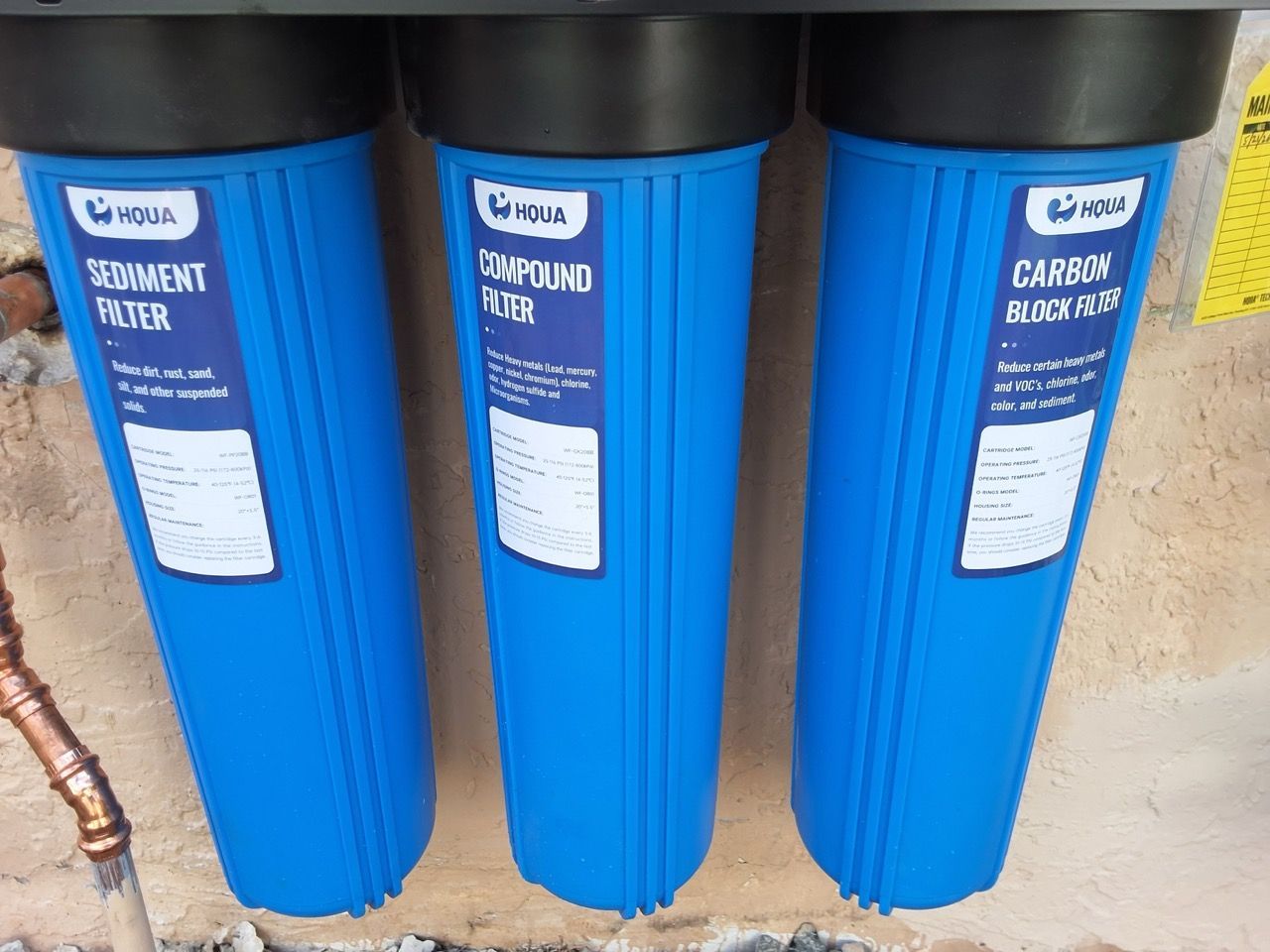 Three blue whole-house water filter housings with black tops lined up against a wall.