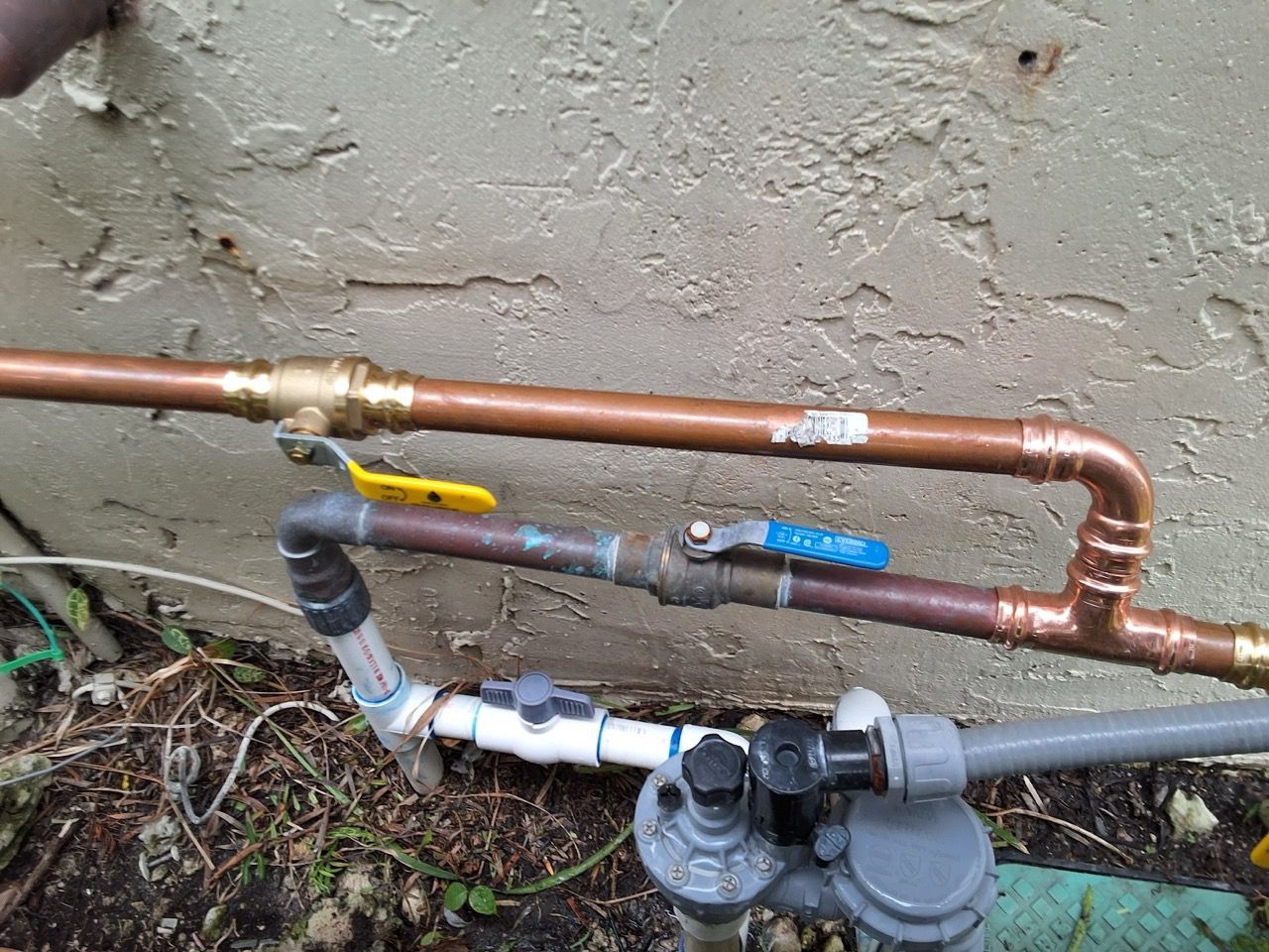Copper and plastic utility pipes with valves and a meter against a stucco wall outdoors