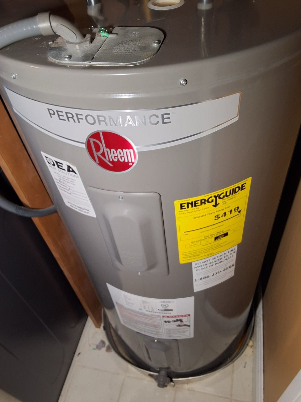 Water heater with yellow warning label and red logo, viewed in a utility closet.