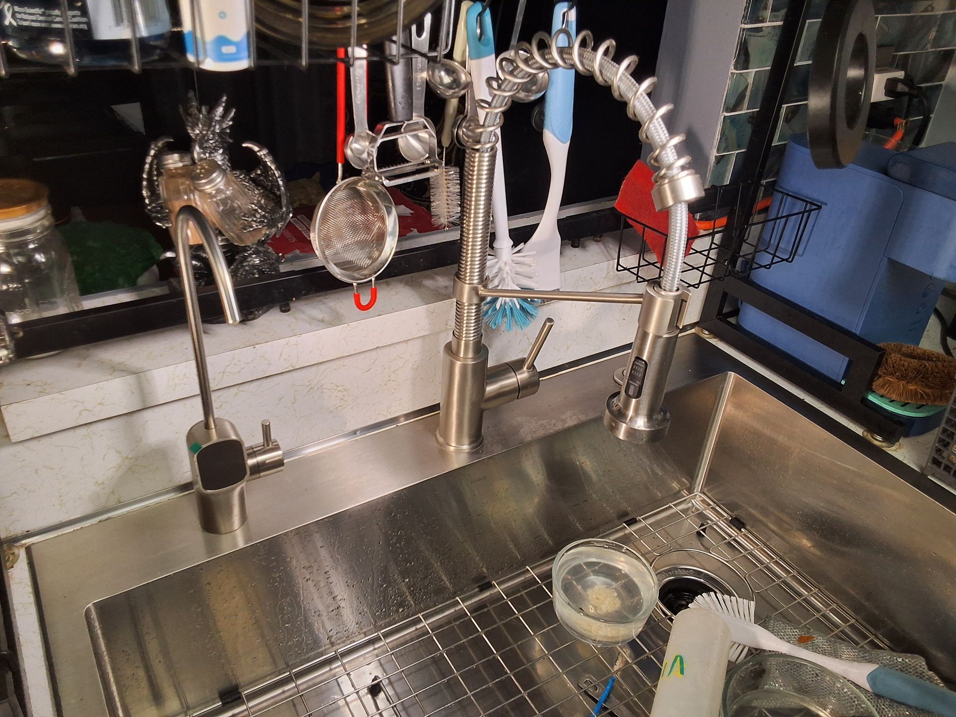 Stainless steel kitchen sink with faucet, sprayer, and dish rack, with a cup and dishes inside