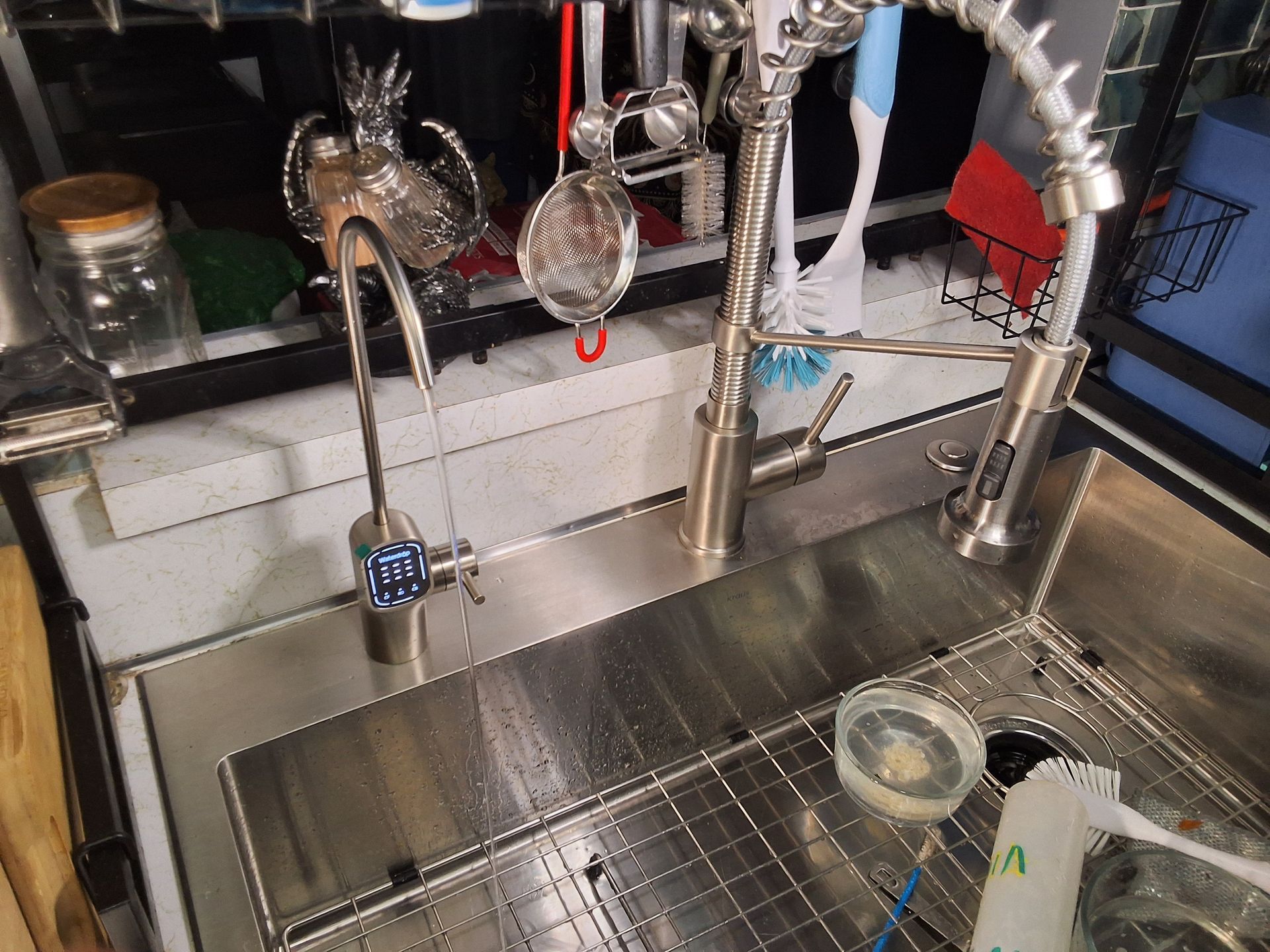 Stainless steel kitchen sink with two arched faucets and a dish rack beside it.