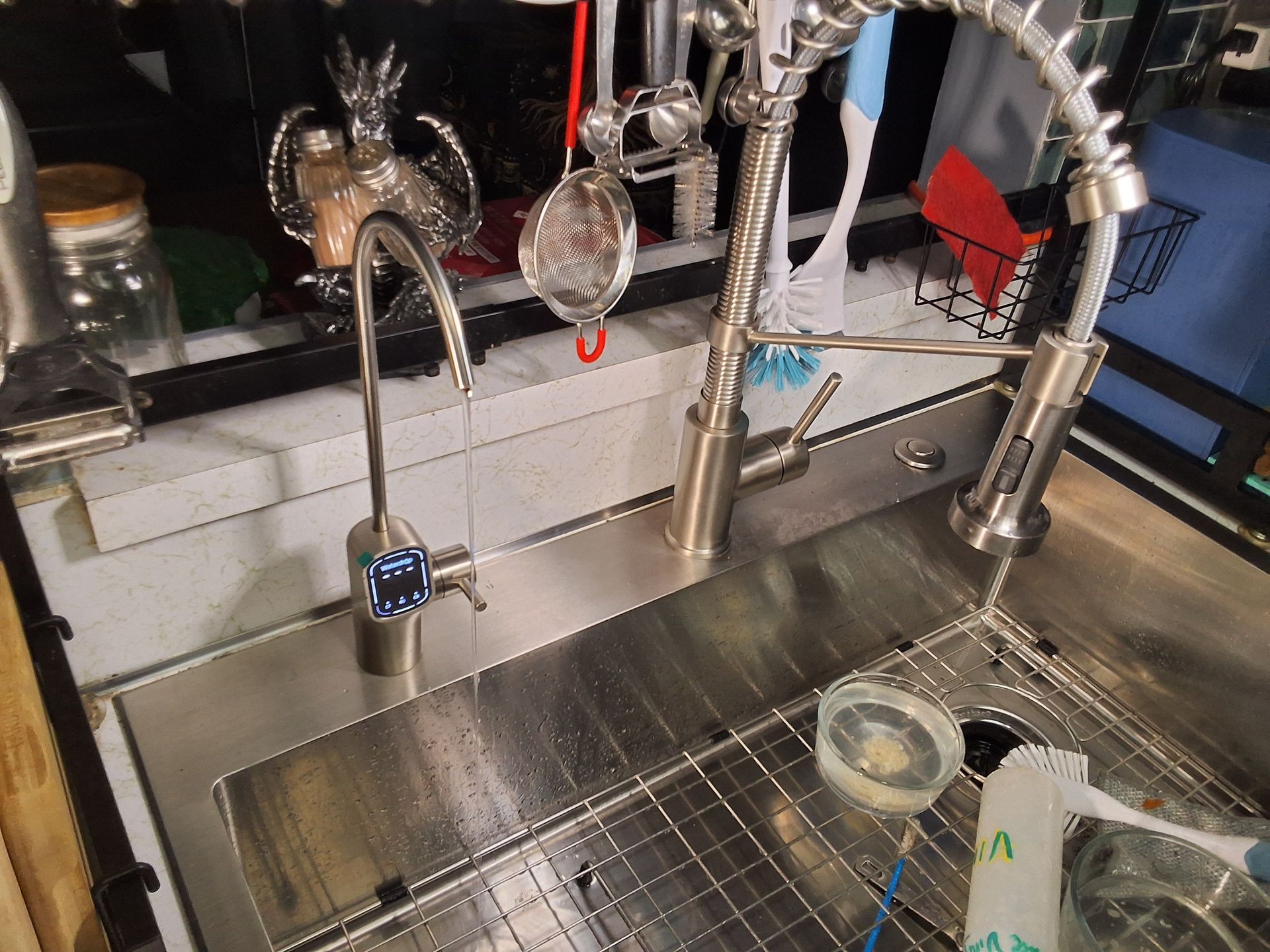 Stainless steel kitchen sink with modern faucet, soap dispenser, and dish rack under bright light