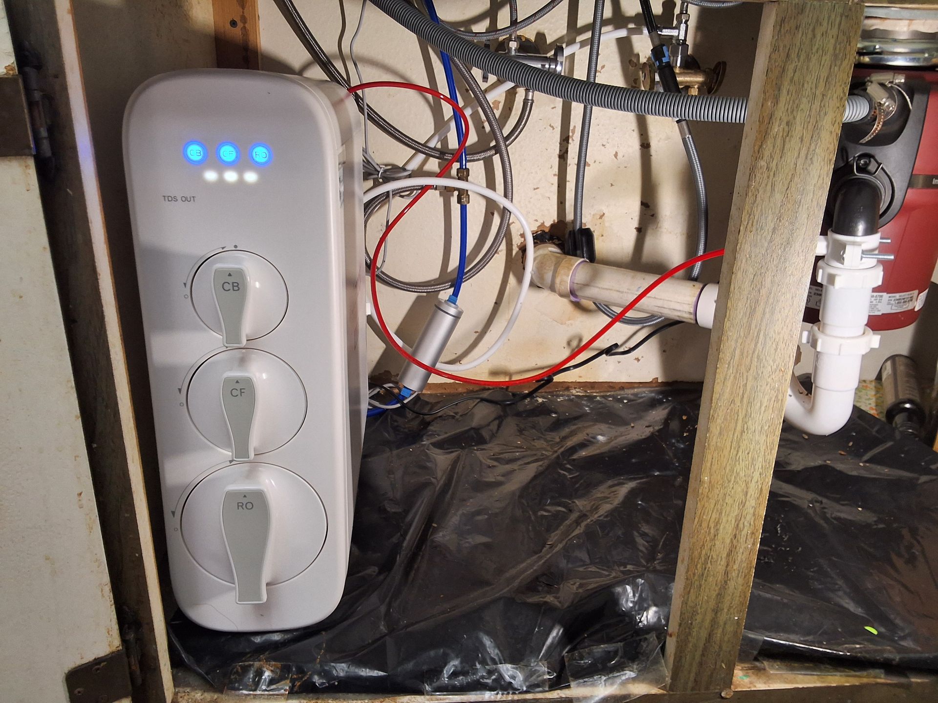 Wall-mounted white control panel with blue lights in a utility space with exposed pipes and wiring