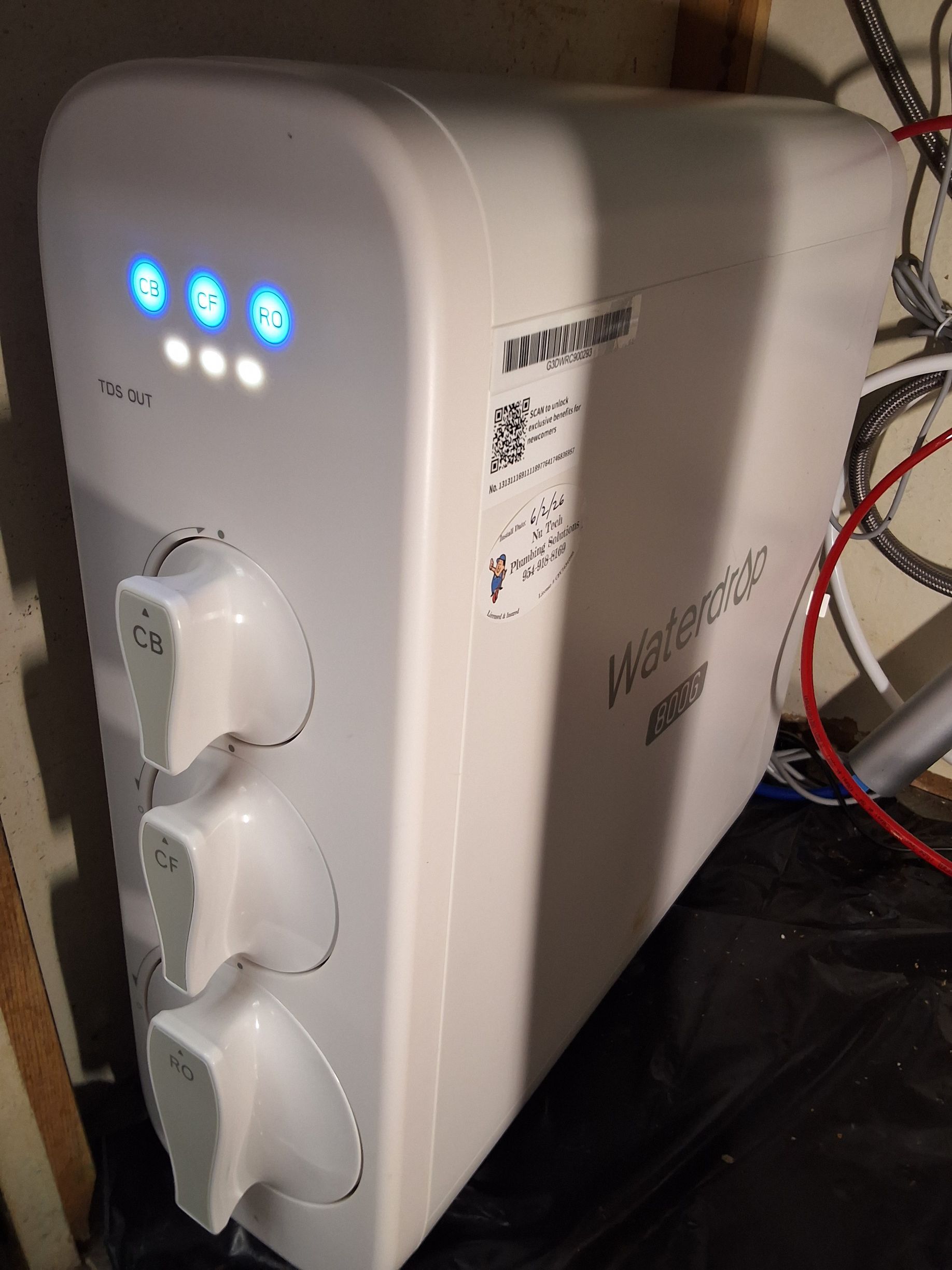 White appliance with three blue indicator lights and three front dials on a tabletop near tangled wires