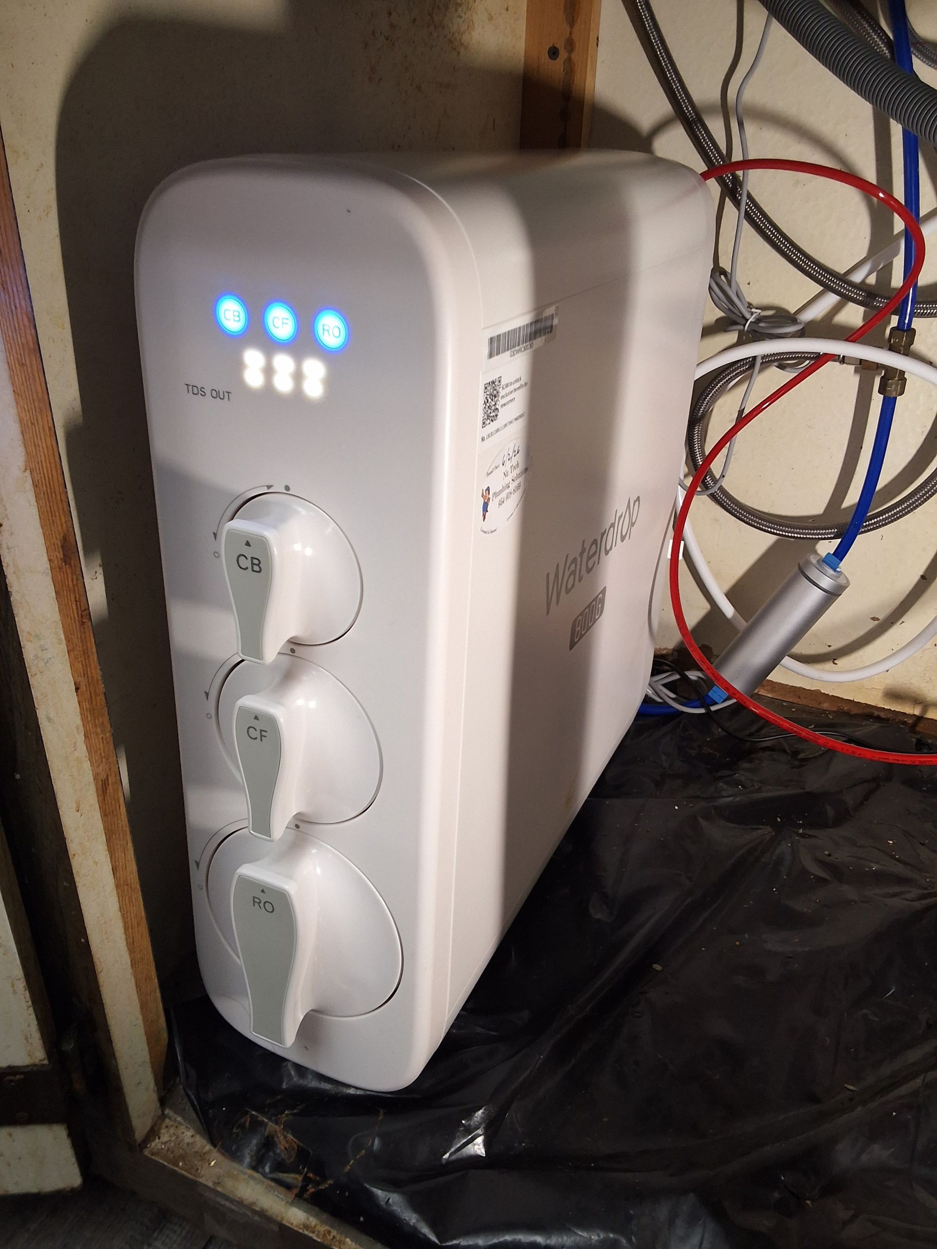 Electrical meter panel with exposed copper pipes and three white filter canisters on a wall indoors