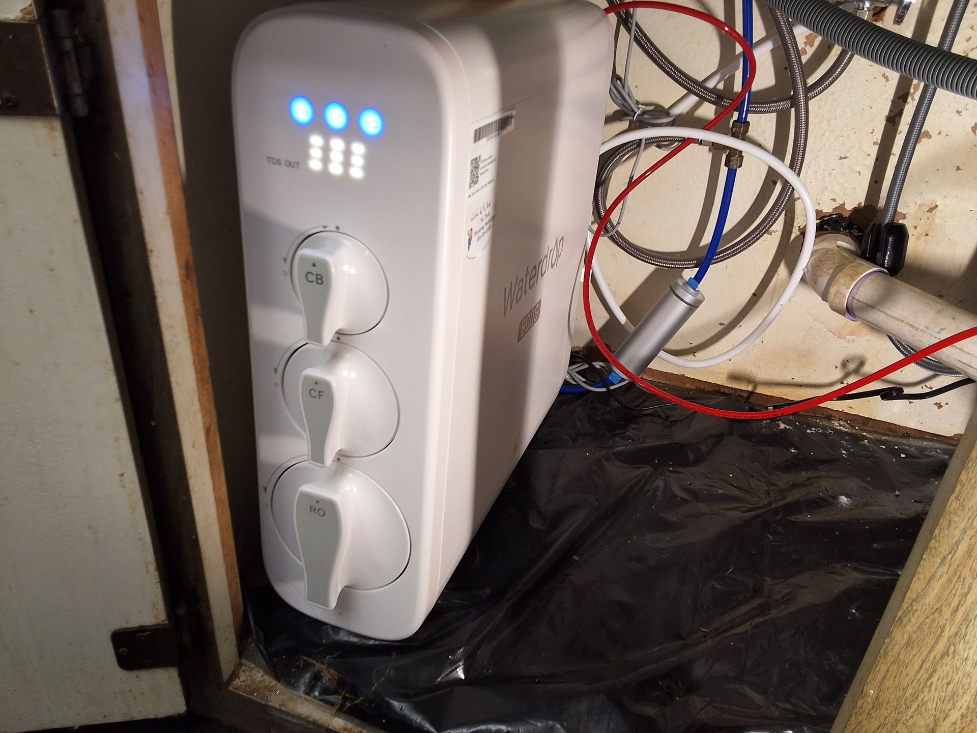 White power strip with blue indicator lights and three plugs in a cluttered wired cabinet.