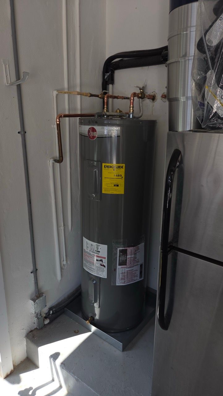 Water heater in a utility closet with exposed pipes and nearby ductwork.