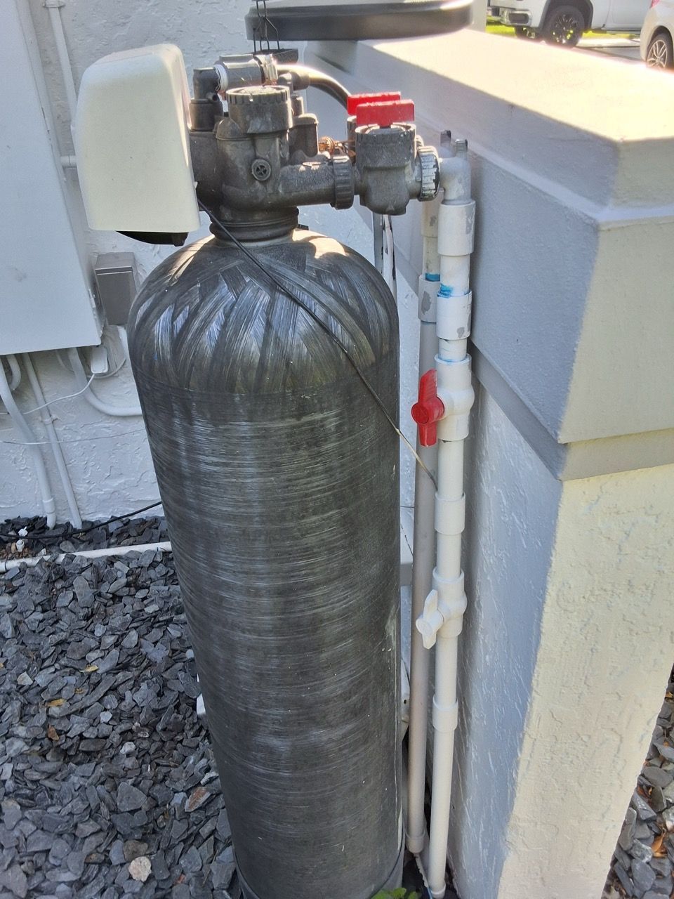 Water softener tank with plumbing and control valve beside an exterior wall.