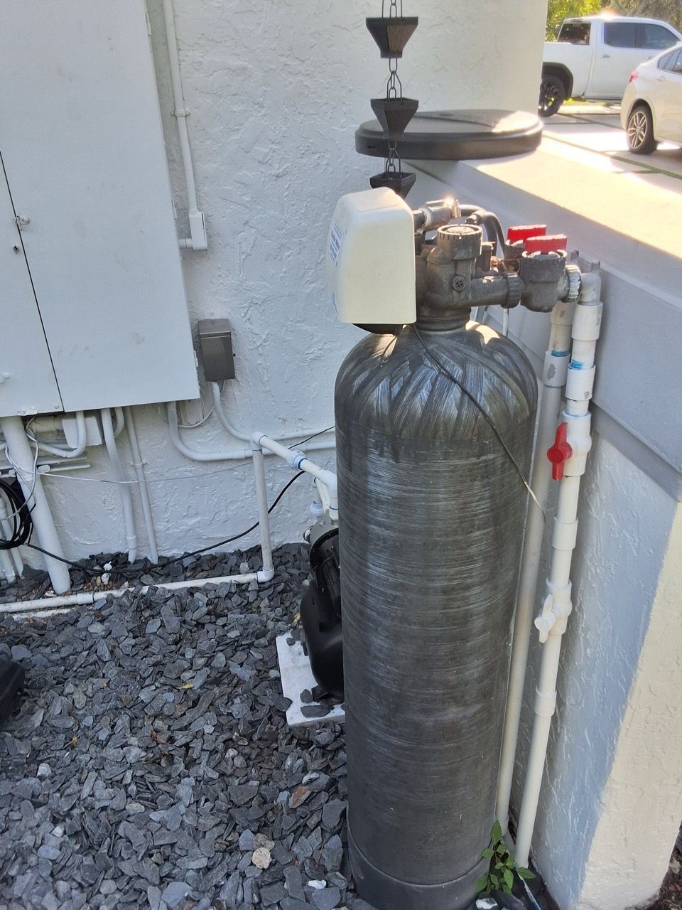 Water filtration tank and plumbing equipment beside a building wall outdoors