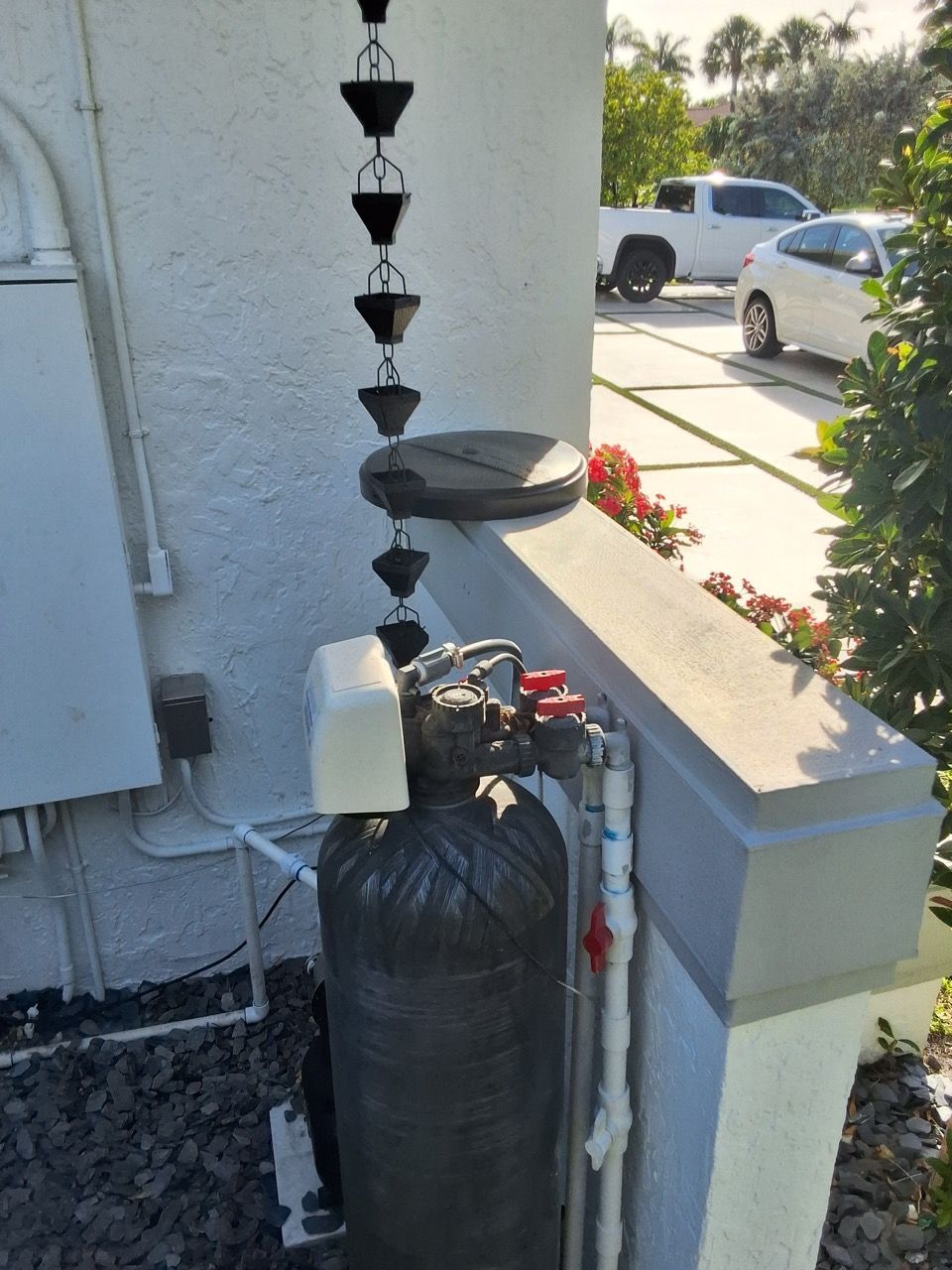 Outdoor water filtration tank beside a house, with a black cylindrical filter and hanging black cone ornaments.