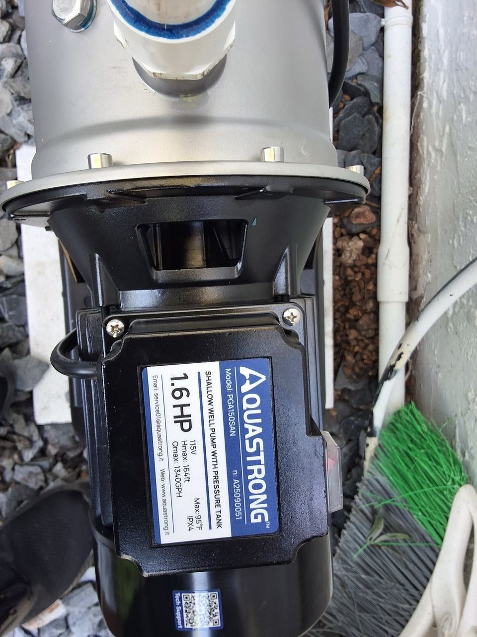 Black AQUASRONG 1.6HP pump mounted under a silver pipe outdoors among rocks and a broom