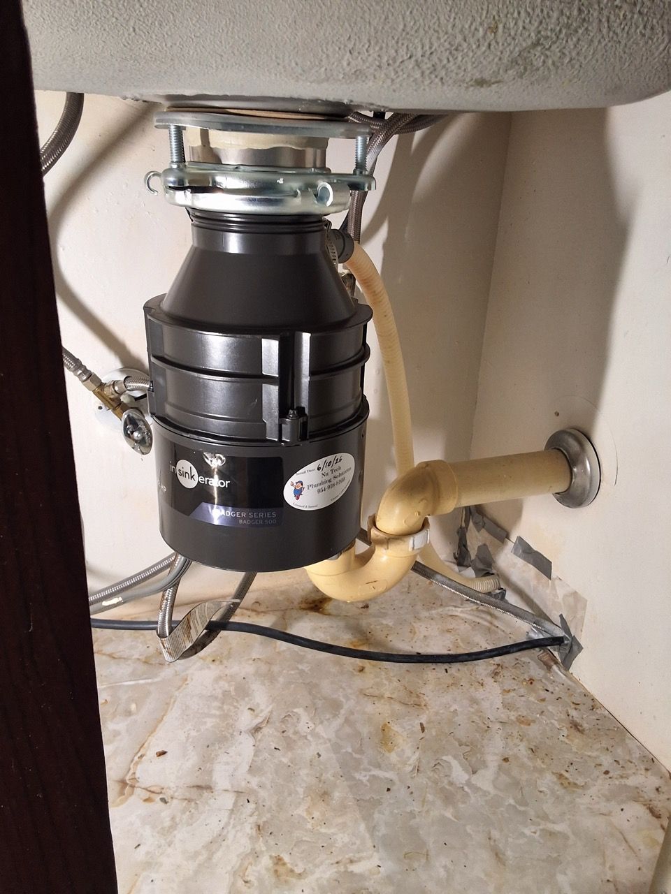 Under-sink garbage disposal with beige drain pipe and wiring in a cabinet under a sink
