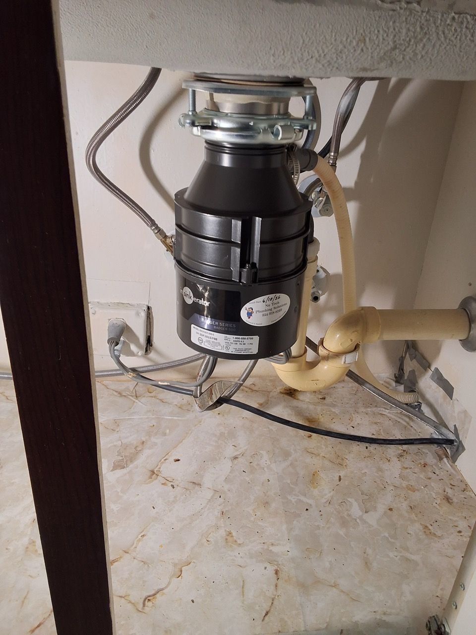 Under-sink garbage disposal with exposed plumbing and electrical wiring.
