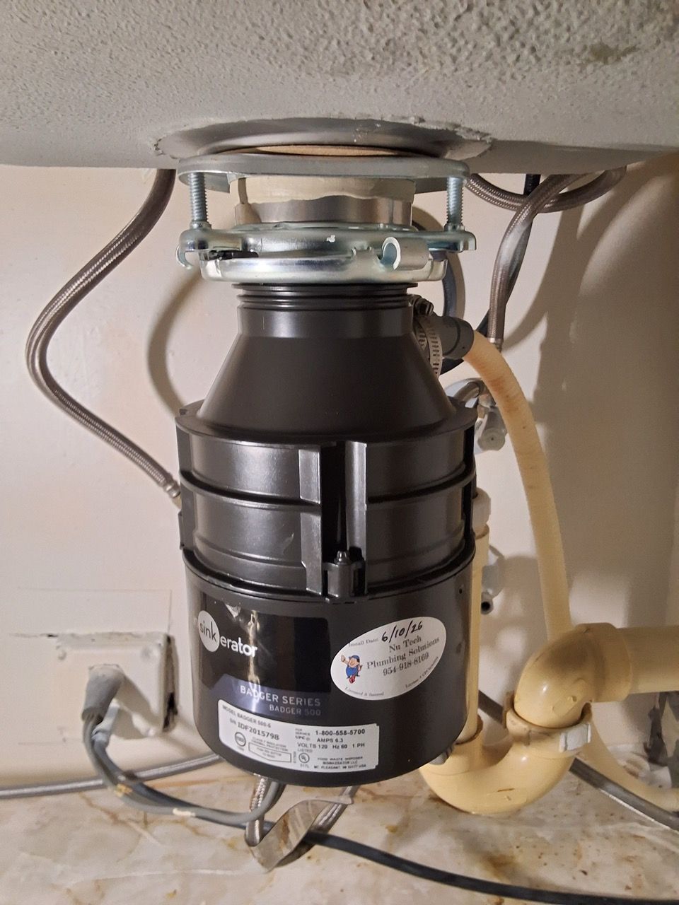 Under-sink garbage disposal unit with pipes and wiring in a kitchen cabinet.